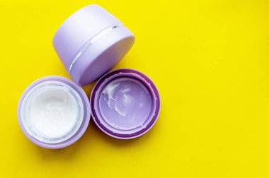 Sarı arka planda yüz kremi olan gri kavanozlar. Cilt bakımı.