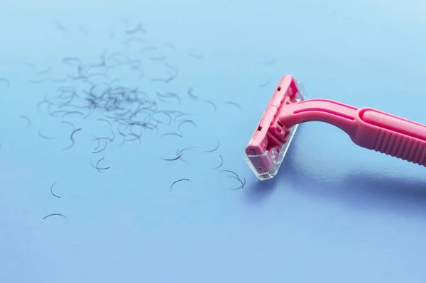 Kobieca maszyna do golenia różowa i włosy na niebieskim tle. Koncepcja golenia kobiet. — Zdjęcie stockowe