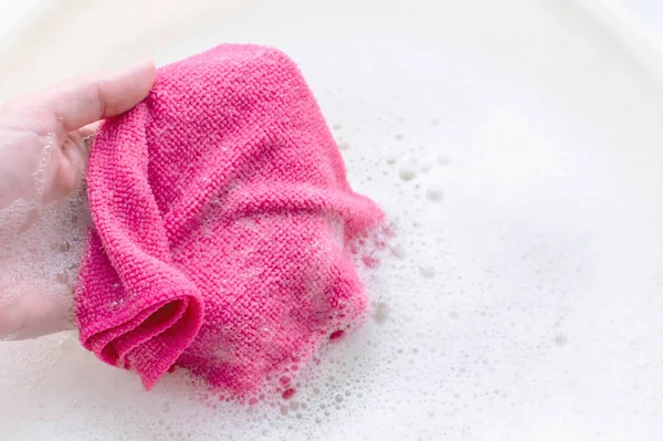 Household rag in hand on the background of soap suds. The concept of household. — Stockfoto