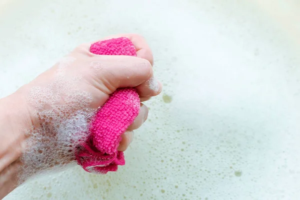 Household rag in hand on the background of soap suds. The concept of household. — Stockfoto