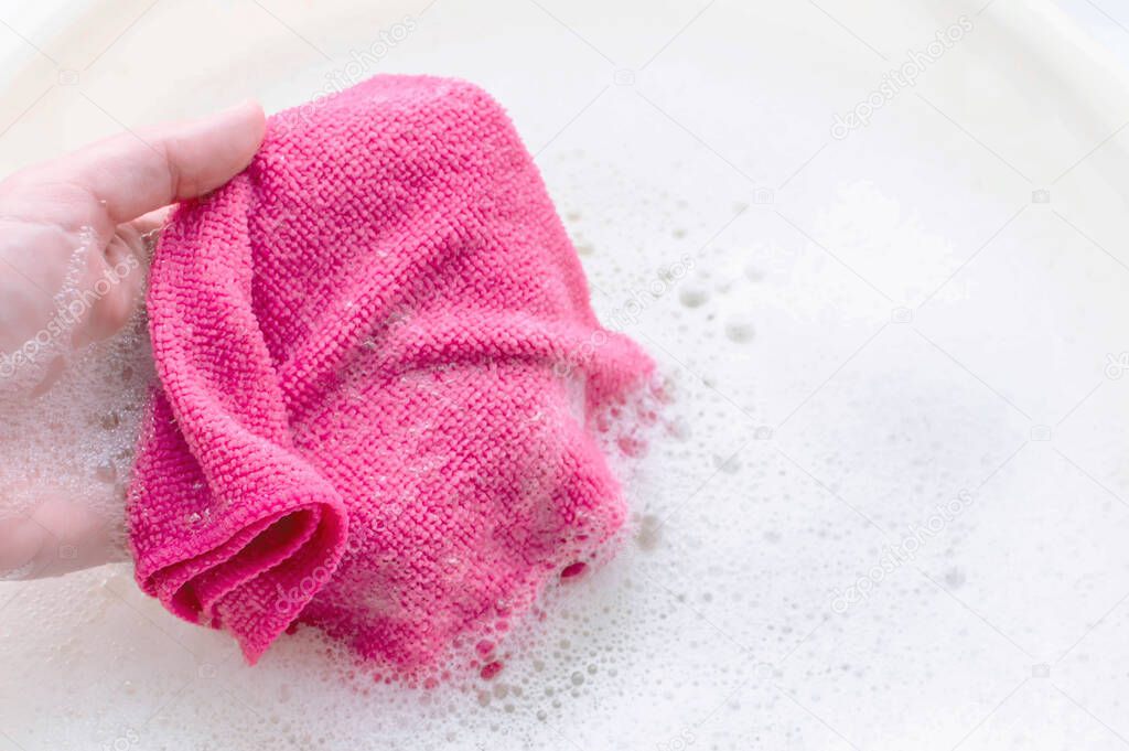 Household rag in hand on the background of soap suds. The concept of household.