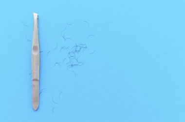 Mavi arka planda kaş ve saç koparmak için cımbız ve yazı yazmak için bir yer.