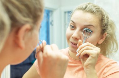 Kadın kirpikleri maşayla düzeltiyor, kapat. Seçici odak, film tahılları.