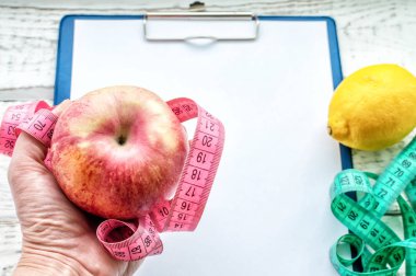 a red Apple and a centimeter-long ribbon in a woman's hands against the background of a notebook. diet, healthy body, proper nutrition.