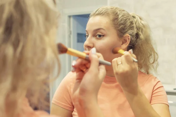 La chica en el espejo con un cepillo en las manos pone rubor en su cara. De cerca. enfoque selectivo. grano de película . — Foto de Stock