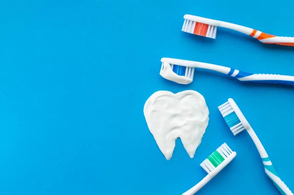 Multi-colored toothbrushes on a blue background with a tooth pattern drawn with toothpaste. The view from the top.The concept of dental health.