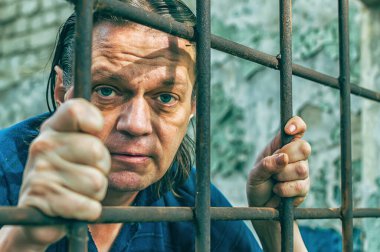 Parmaklıklar ardında elleri kelepçeli depresif bir adam. Depresyonda olan bir erkek suçlu hapse atıldı. Haykırıyor, kırıyor, ağlıyor.