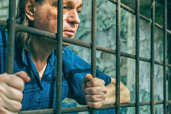 A depressed man holds his hands on the prison bars. Prisoner for the crime. Poor conditions. Scream, despair, pain, hunger.