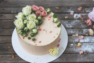Pasta tezgahında taze çiçeklerle süslenmiş pembe kremalı pasta ahşap bir masanın üzerinde duruyor. Seçici odaklanma. Kapat..