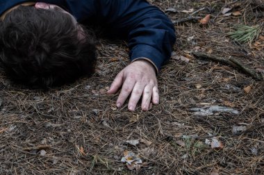 Ormanda cinayet. Mavi gömlekli bir adamın bedeni ormandaki ağaçların arasında yerde yatıyor. Bir saldırı kurbanı. Yatay fotoğraf.