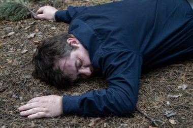 Ormanda cinayet. Mavi gömlekli bir adamın bedeni ormandaki ağaçların arasında yerde yatıyor. Bir saldırı kurbanı. Yatay fotoğraf.