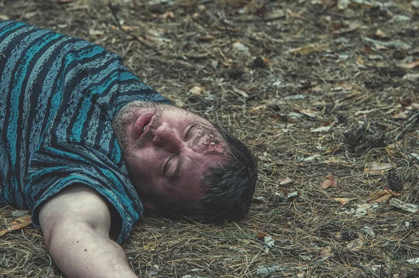 Murder in the woods. The body of a man in a blue t-shirt lies on the ground among the trees in the forest. Victim of an attack. Horizontal photo.
