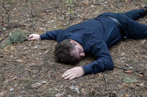Murder in the woods. The body of a man in a blue shirt and trousers lies on the ground among the trees in the forest. Victim of an attack. Horizontal photo.