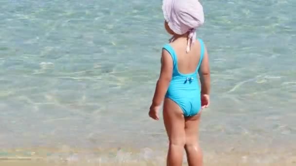 Маленька дівчинка в блакитному купальнику грає на пляжі — стокове відео