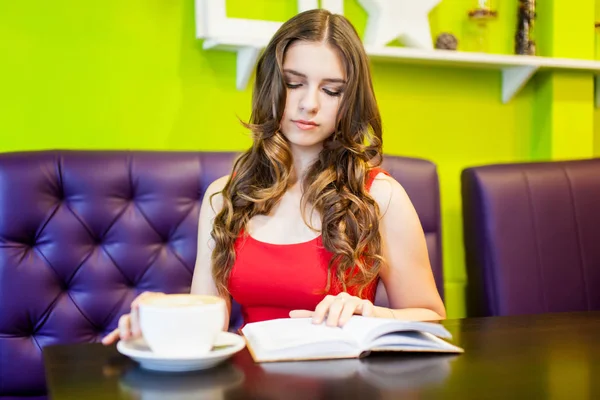 Uma jovem mulher bonita está bebendo café em um café — Fotografia de Stock