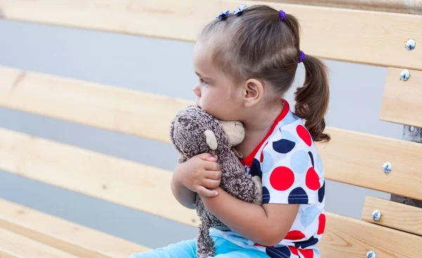 Девушка сидит на скамейке и обнимается с игрушкой обезьяны — стоковое фото