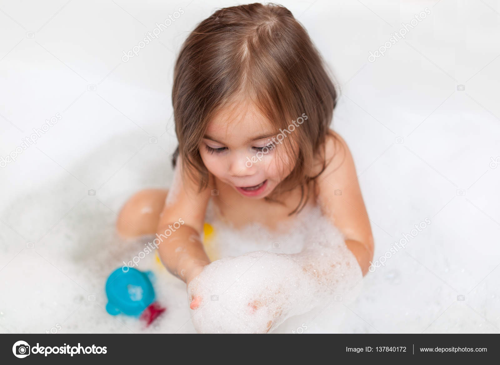 Funny baby girl playing with water and foam Stock Photo by