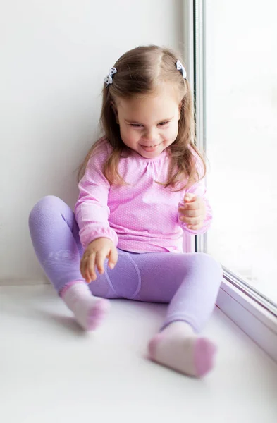 Cute little girl sitting on the windowsill — Stock Photo, Image