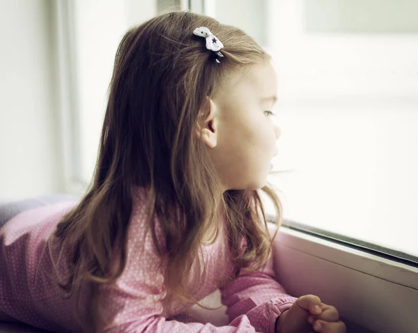Nettes kleines Mädchen auf der Fensterbank liegend — Stockfoto