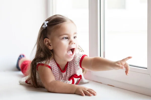 Little smiling child girl watching out the window — Stock Photo, Image