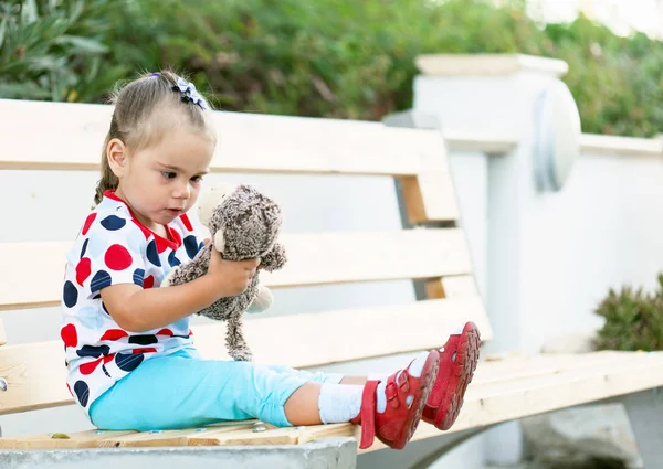 girl sitting on the bench and cuddling monkey toy
