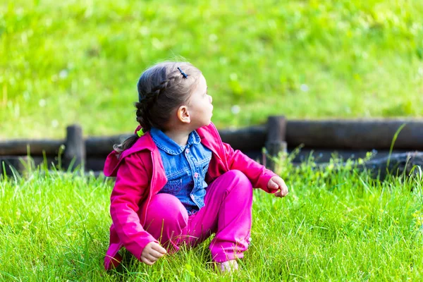 Ευτυχισμένο παιδί κορίτσι που κάθεται στο πράσινο γρασίδι — Φωτογραφία Αρχείου