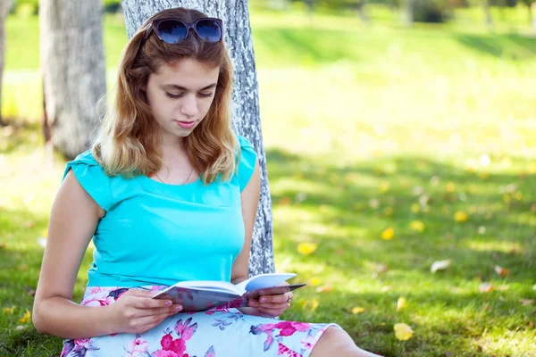 Adolescente sentada na grama e lendo livro — Fotografia de Stock