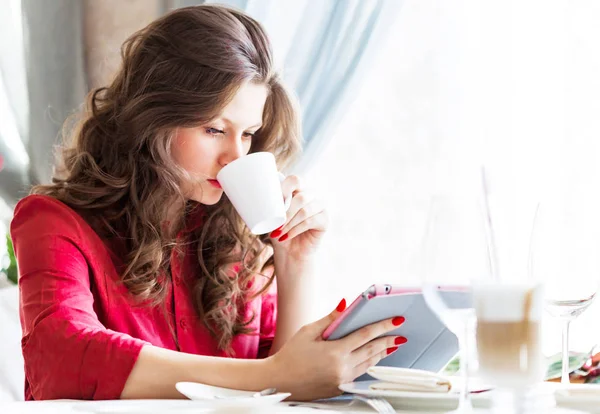 Beautiful woman in city cafe. She id drinking coffee and using her tablet — Stock Photo, Image