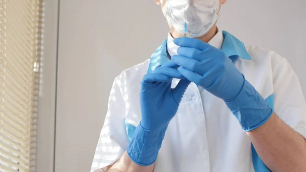 Врач в медицинской маске и синих перчатках готовится к инъекции. — стоковое фото