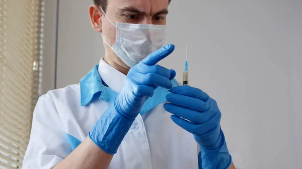 Tıbbi maskeli ve mavi eldivenli doktor iğneye hazırlanıyor.. — Stok fotoğraf