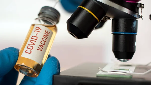 Врач или лаборант держит трубку с ковидовой вакциной и микроскопом . — стоковое фото