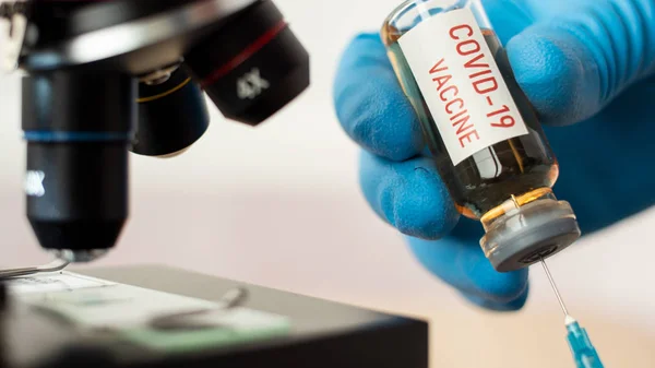 Врач или лаборант держит трубку с ковидовой вакциной и микроскопом . — стоковое фото