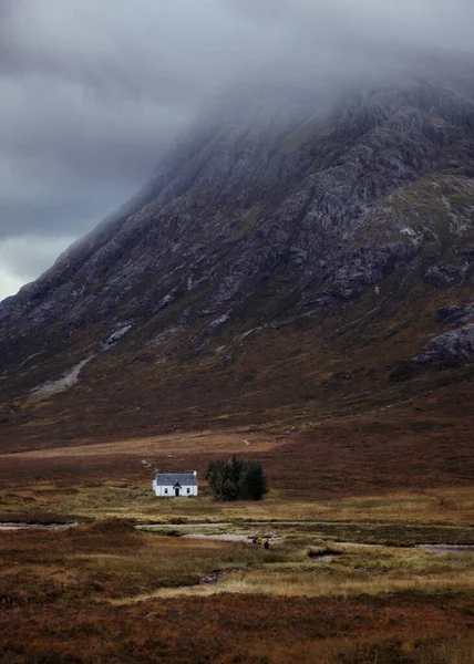 Samotna biała chata stojąca w pobliżu ogromnej góry pokrytej clou — Zdjęcie stockowe