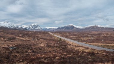 Glen Coe 'nun İskoç Dağları' ndan geçen bir yolun manzarası, karlı dağlar ve vadi. İskoçya