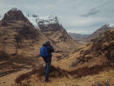Sırt çantalı bir adam dağdan dağ vadisine bakıyor. Aktif rahatlama, motivasyon ve hedefe ulaşma kavramı. Glencoe, İskoçya, İngiltere.
