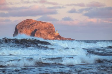 Fırtına dalgaları ve deniz feneri gün batımında bir uçurumda