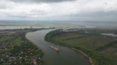 Yukarıdan mavnalı olan bir nehir. Köy, yeşil çayırlar ve tarlalar, yağmur bulutları.