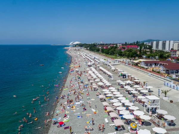 Strand, emberek úszás és napozás, tiszta kék víz, tengerpart, színes szőnyegek, fehér strand esernyők. Kilátás felülről. Stock Kép