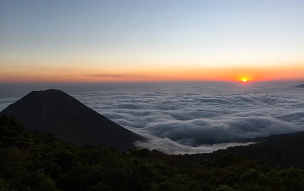 De vulkaan Izalco stijgt boven wolken bij zonsondergang — Stockfoto