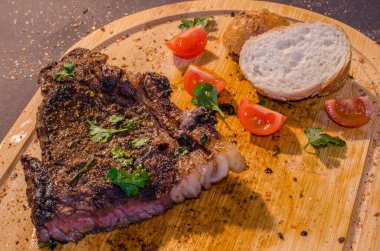 Kavrulmuş domuz biftek üzerine maydanoz, domates ve ahşap kesme tahtası, yan görünüm üzerinde Fransız ekmeği ile
