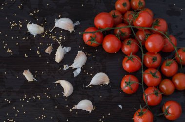 Kiraz domates ve sarımsak, dökülen baharatlar ile siyah arka plan üzerine