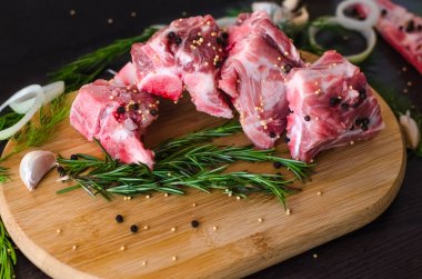 Taze çiğ et kemik ve biberiye, sarımsak ve baharat siyah zemin üzerine ahşap kesme tahtası üzerinde kara biber