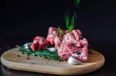 Taze çiğ et kemik ve biberiye, sarımsak ve karabiber, baharat siyah zemin üzerine ahşap kesme tahtası üzerinde otlar düşüyor