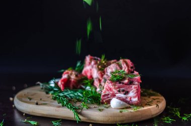 Et ve biberiye, sarımsak ve karabiber, baharat siyah zemin üzerine ahşap kesme tahtası üzerinde düşen otlar