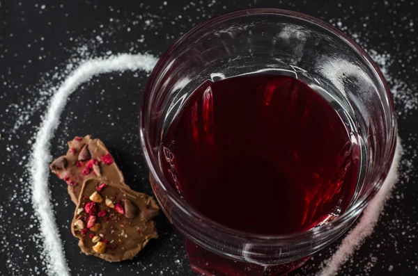 Berries tea in glass, spilled sugar in shape of heart around, milk chocolate, on black background