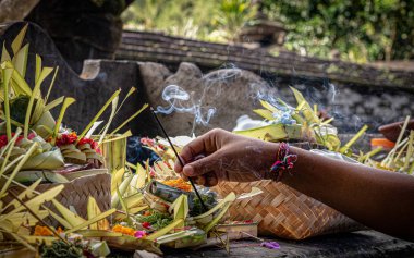 Bali tapınağındaki bir adağa yanan tütsü koyan bir el.