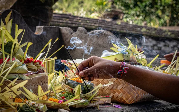 Bali tapınağındaki bir adağa yanan tütsü koyan bir el.