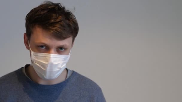 Een man met een chirurgisch masker met griep die in de camera kijkt. — Stockvideo