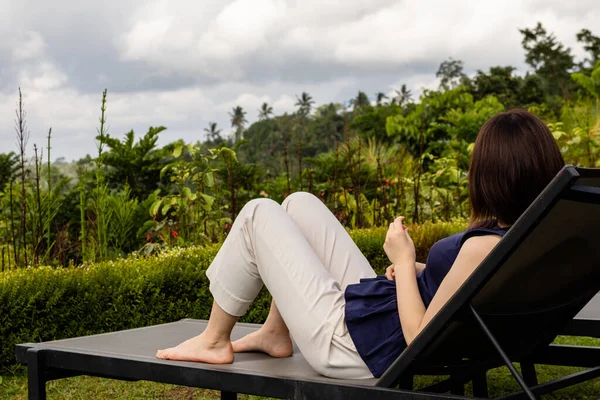 Genç bir kadın tropikal bir yerde iskemlede dinleniyor.