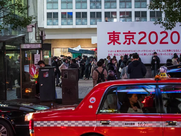 Shibuya, Japan - 7.2.20: En rød drosje passerer foran folk som venter på å krysse Shibuya – stockfoto